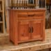 Mueble auxiliar de madera de estilo rústico con un cajón superior, dos puertas y tiradores metálicos, fabricado artesanalmente en un taller de carpintería.